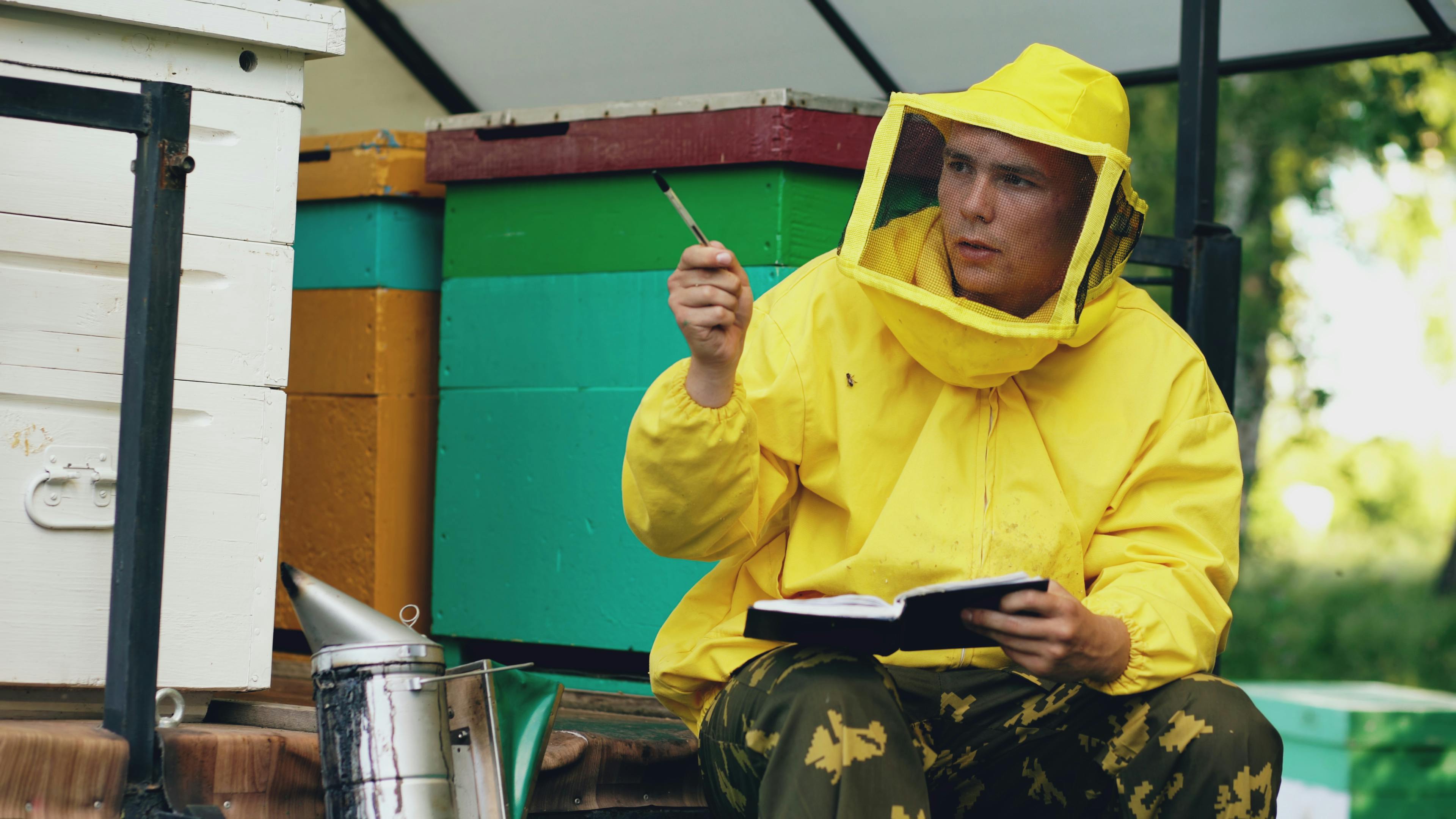 Beekeeper in protective gear inspecting beehives with notes in hand.