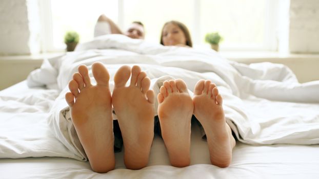 A couple enjoying a relaxed morning in bed with sunlight illuminating the room, creating a cozy atmosphere.