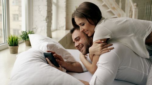 Free Happy couple enjoying time together in bed, viewing tablet indoors. Stock Photo