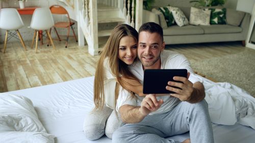 Free A joyful couple relaxing indoors while taking a selfie on a tablet. Stock Photo