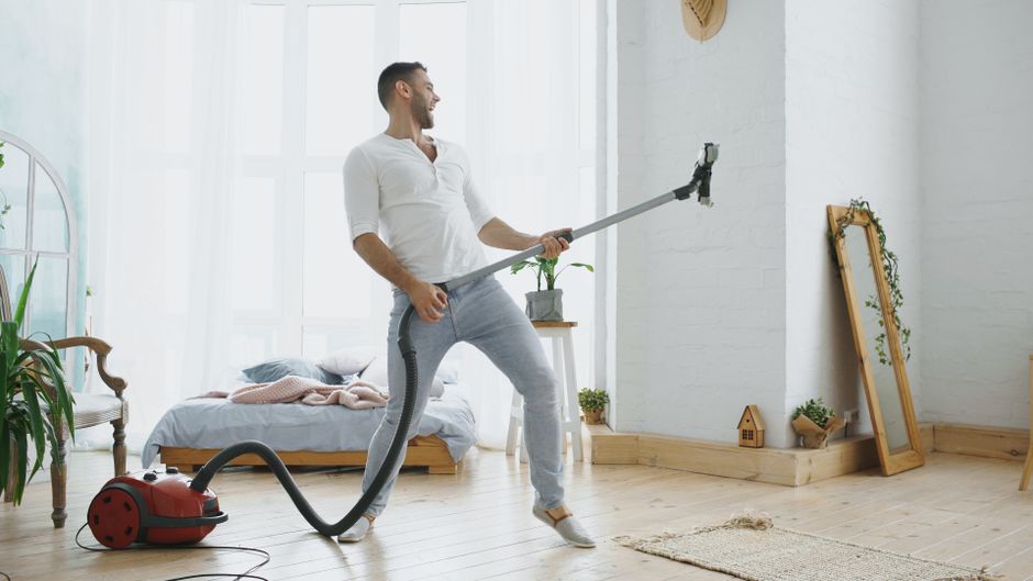 Best Robot Vacuums for Pet Hair in 2025: Ultimate Guide Man enjoying cleaning with vacuum, singing like a rockstar in bright bedroom.