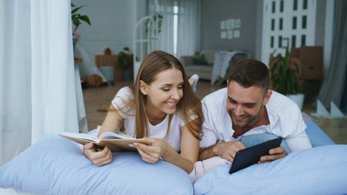 Free Couple enjoying a relaxing moment at home, reading and using a tablet. Stock Photo