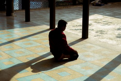 Free A man meditates alone, sitting on a sunlit tiled floor indoors, casting a long shadow. Stock Photo