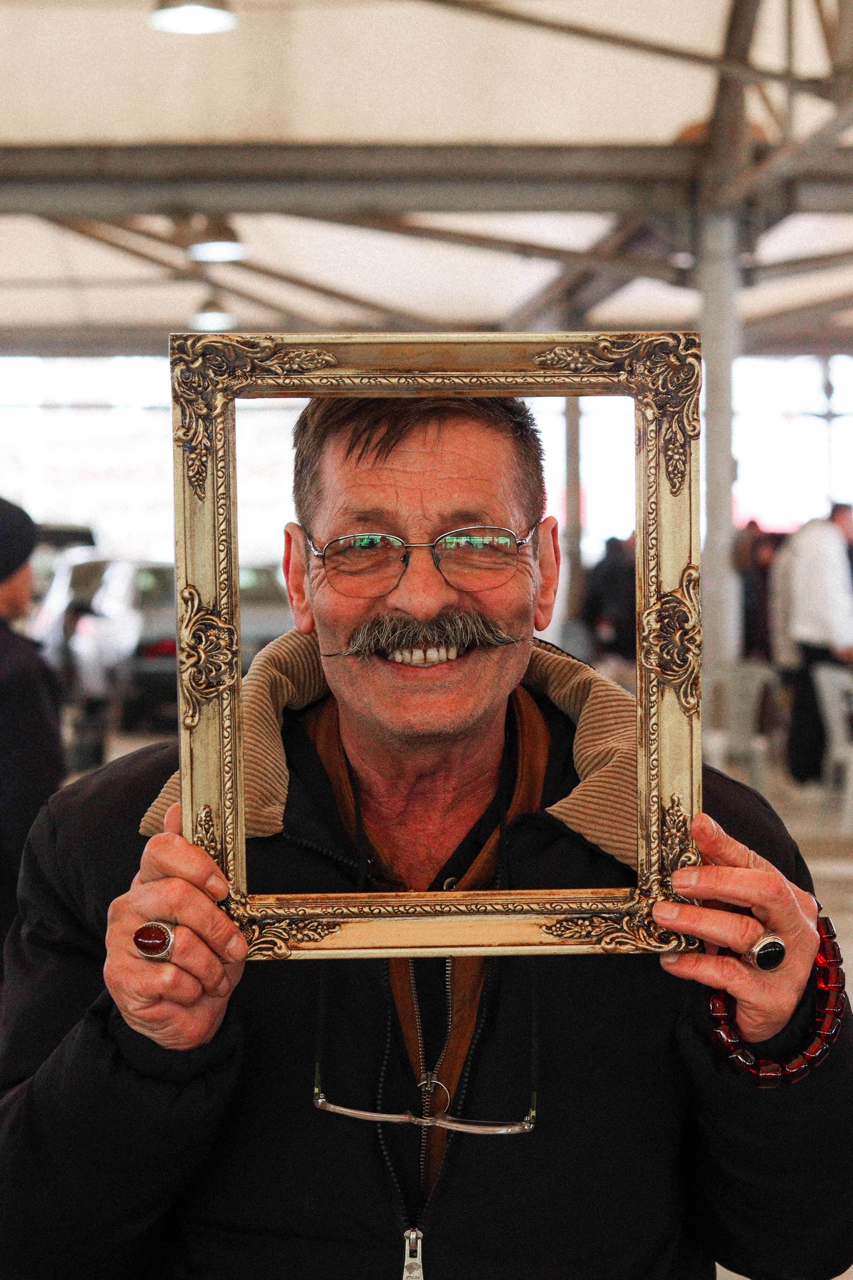 A cheerful man holding a decorative frame in a lively indoor setting.