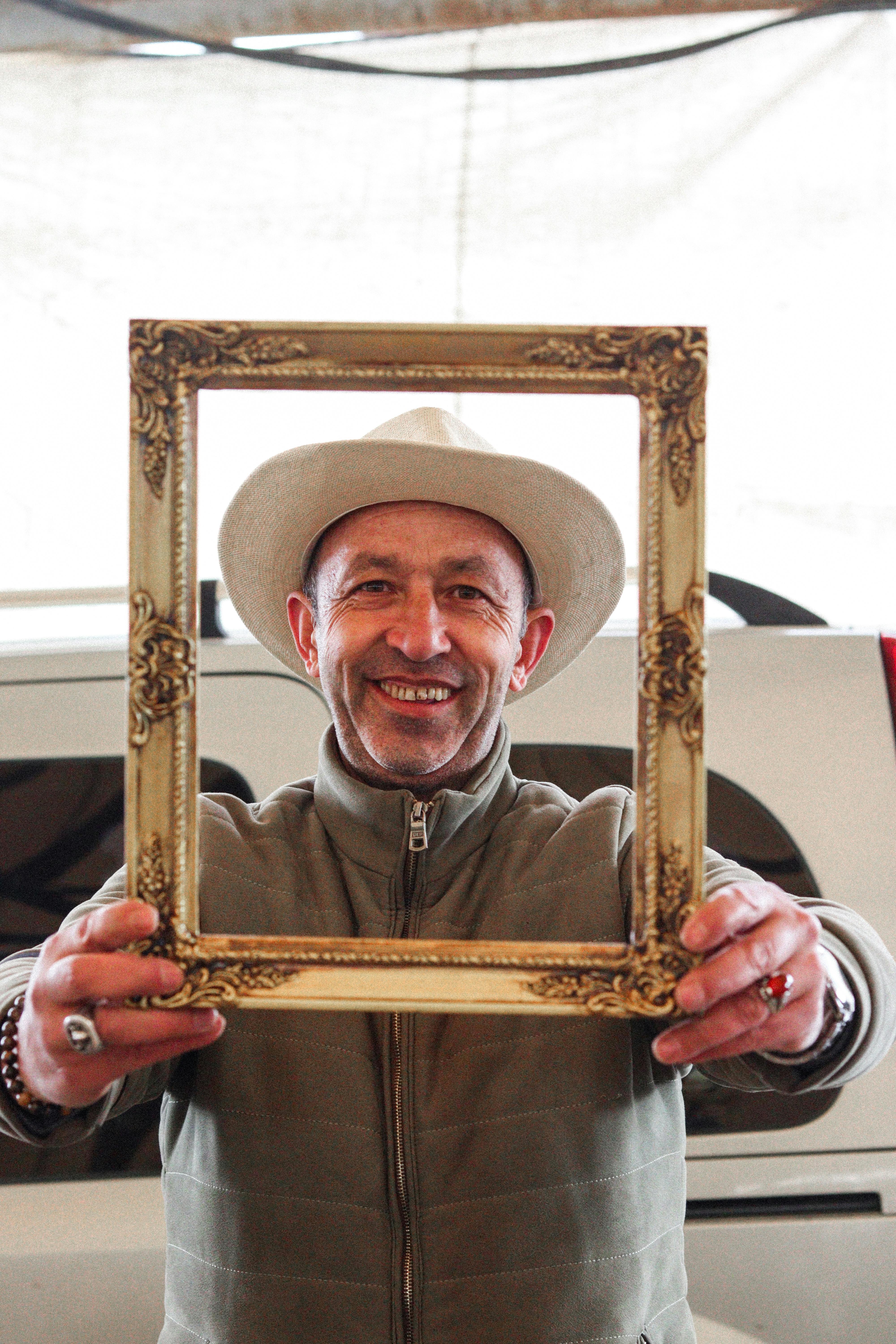 Middle-aged man wearing a cowboy hat holding an ornate picture frame indoors.