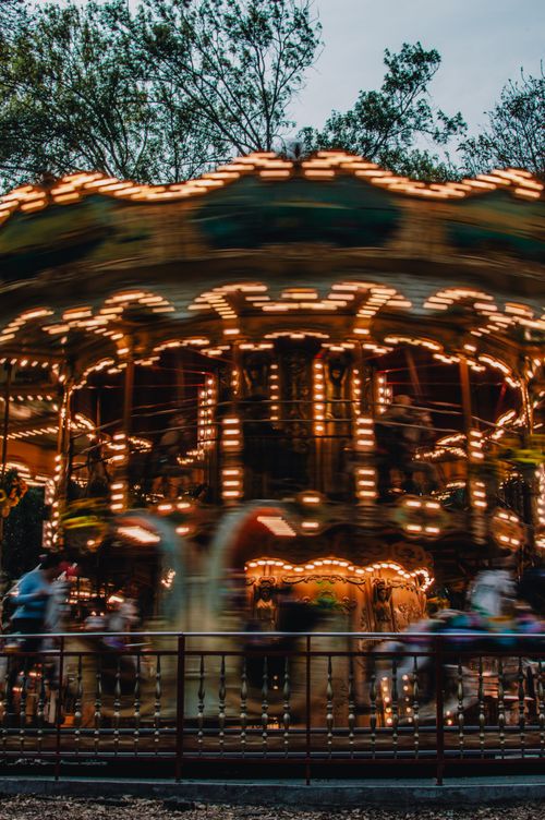 Free A mesmerizing view of a carousel in motion at night, showcasing vibrant lights and blurred figures, capturing the fair's lively atmosphere. Stock Photo