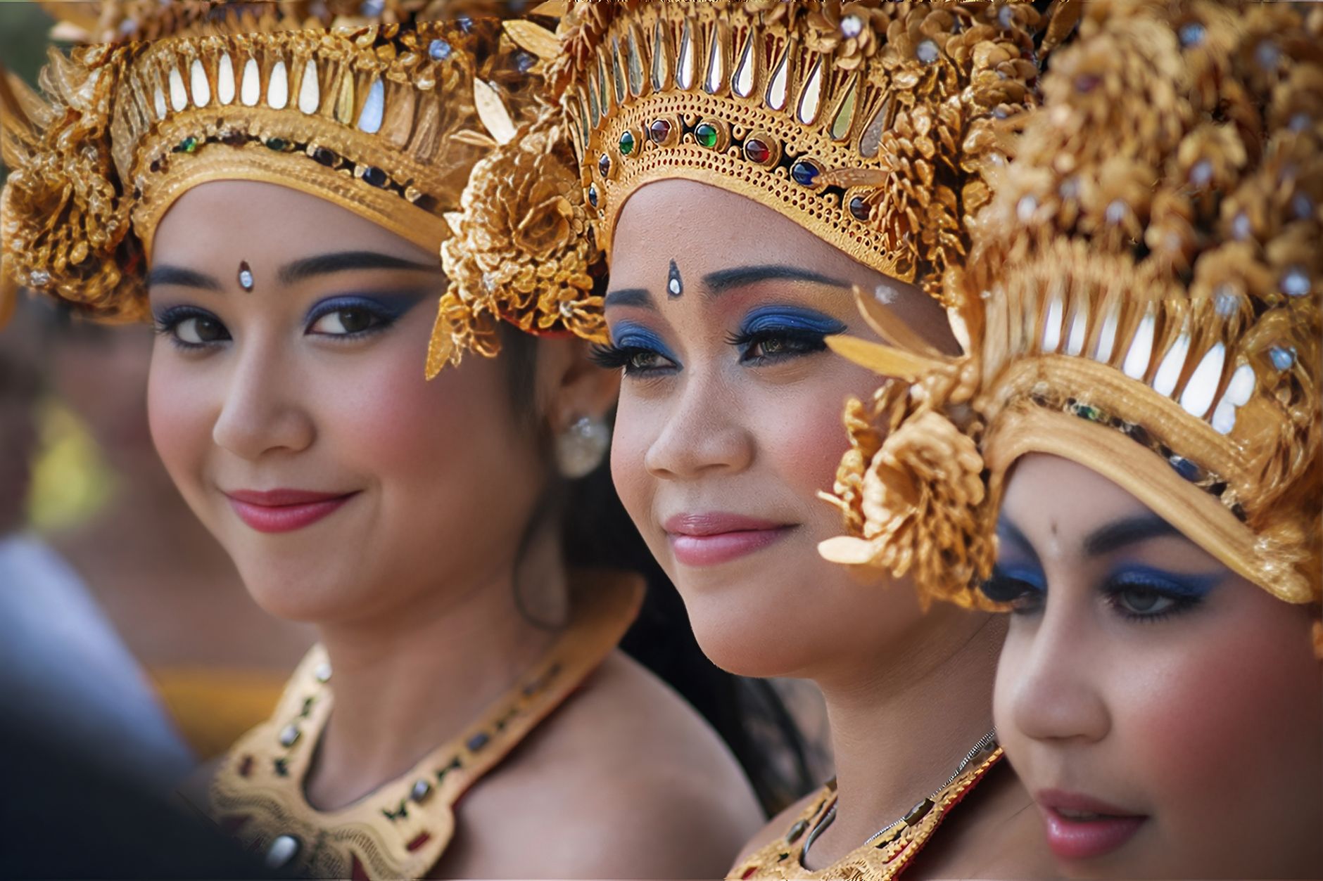 Balinese women adorned in traditional ceremonial dress and jewelry, smiling gracefully.