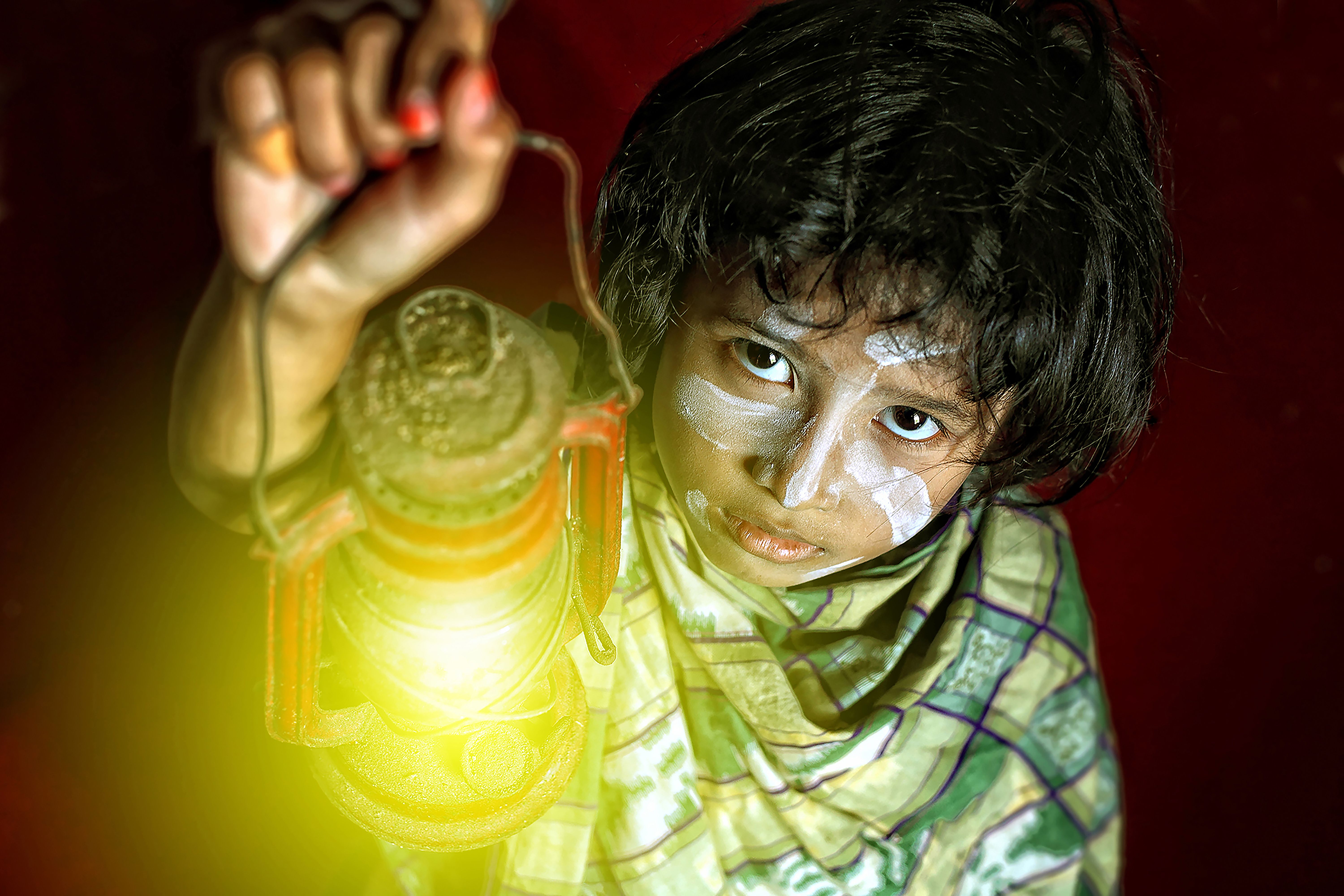 A child in Surabaya with face paint holds a glowing lantern against a red background.