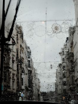 Rainy day view of a city street through a bus window with water droplets.