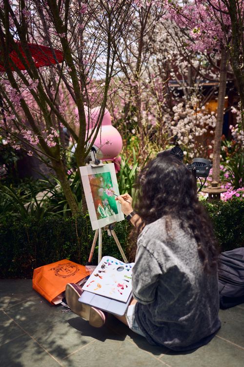 Free A woman paints in a garden surrounded by spring blossoms, capturing the vibrant colors of nature. Stock Photo