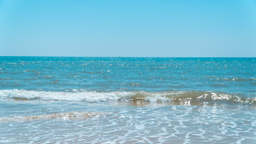 Free Tranquil ocean waves gently touch the sandy shore under a bright blue sky. Stock Photo