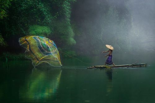 Free A fisherman casting a net on a misty river in Malang, Indonesia, surrounded by lush greenery. Stock Photo