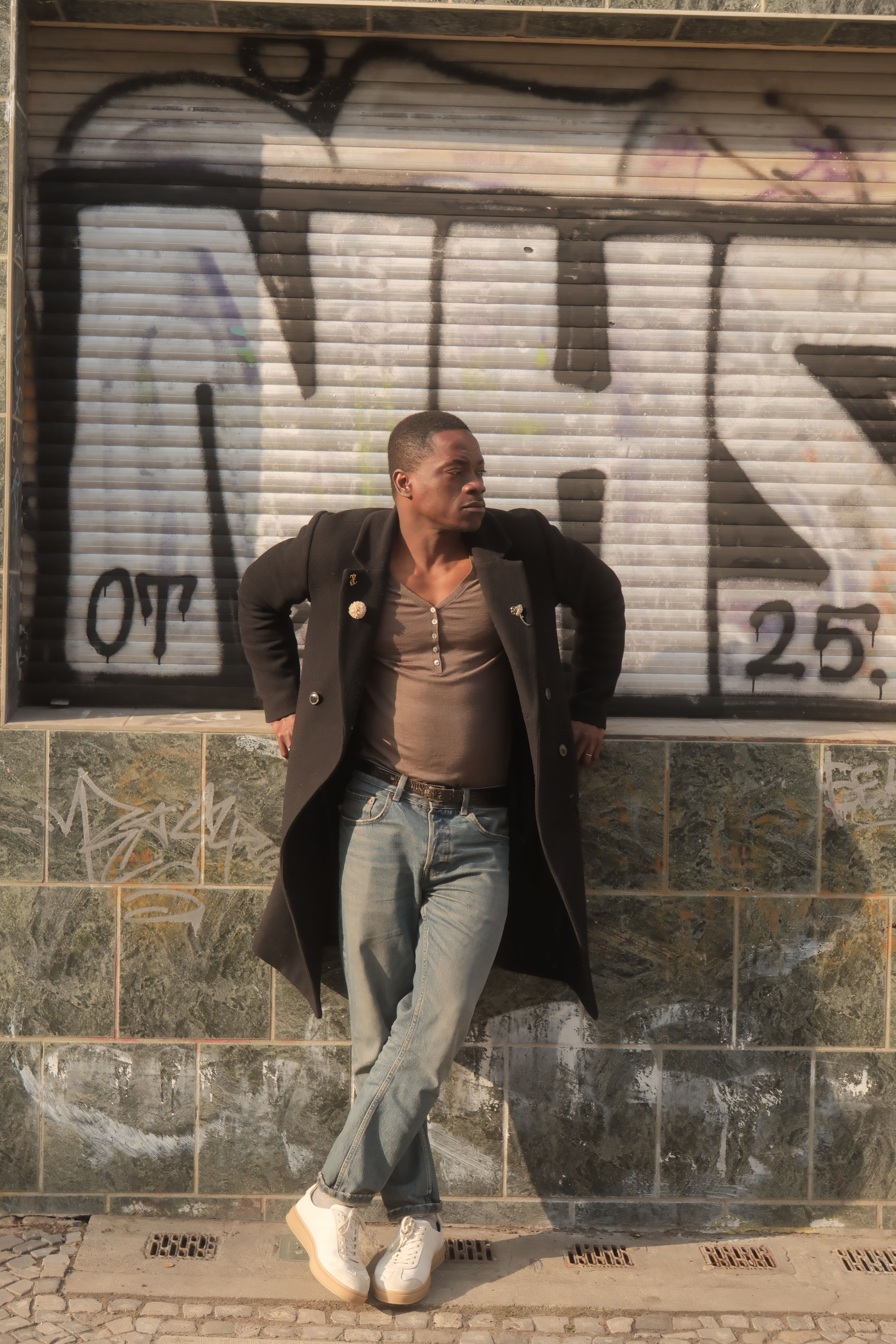Man in a coat and jeans leaning on graffiti-covered wall in Berlin. Urban and stylish.
