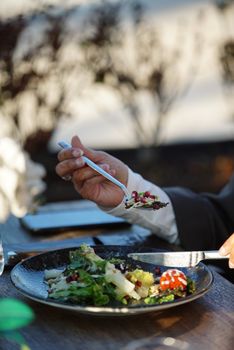 A person enjoys a gourmet salad with their fork and knife at an outdoor setting.