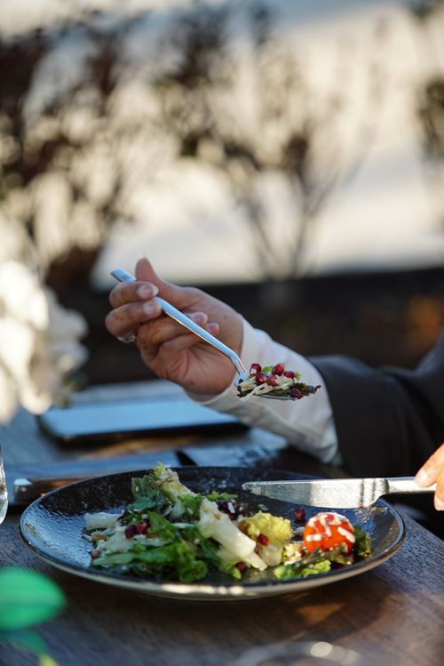 Free A person enjoys a gourmet salad with their fork and knife at an outdoor setting. Stock Photo