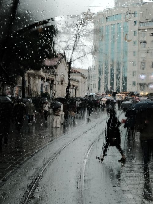 Free View through a wet window capturing a bustling urban street with people in rain. Stock Photo