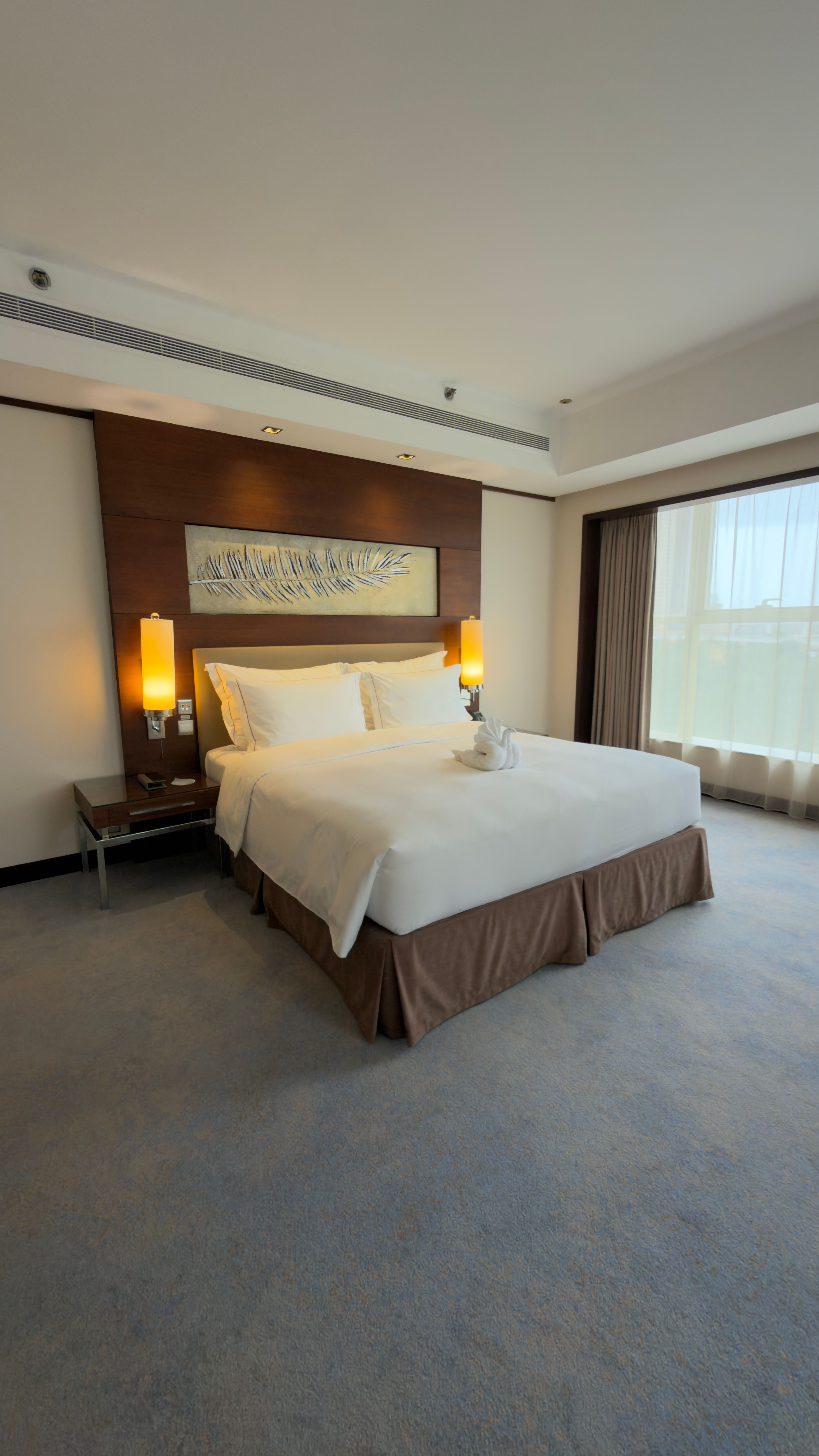 Spacious hotel room featuring a double bed with warm lighting and modern decor.