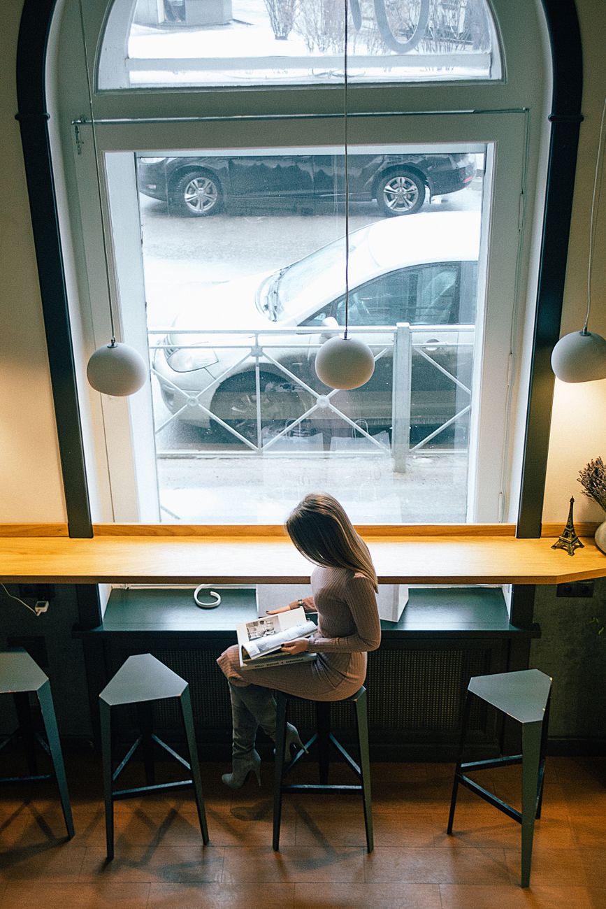A woman reading a magazine in a cozy cafe with large windows on a winter day.. woman, reading, magazine