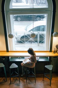 A woman reading a magazine in a cozy cafe with large windows on a winter day.. woman, reading, magazine