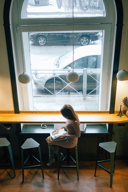 A woman reading a magazine in a cozy cafe with large windows on a winter day.