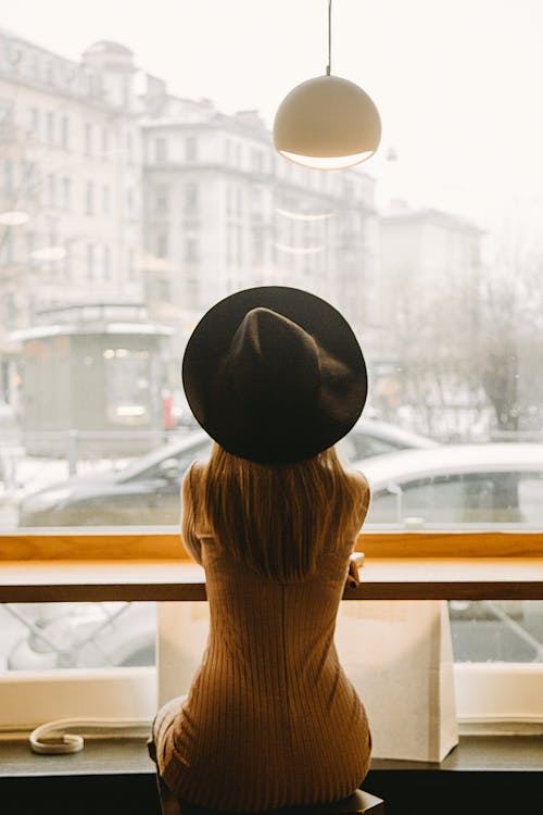 Woman in Black Hat Sitting in Front of Glass Window