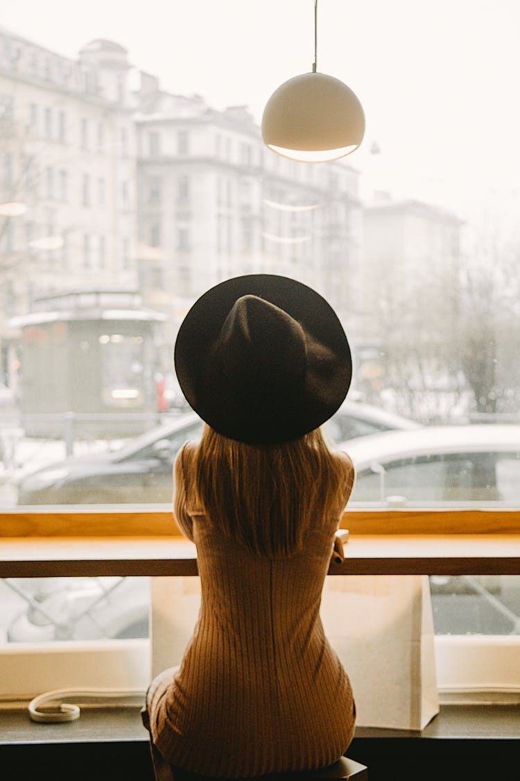 Woman In Black Hat Sitting In Front Of Glass Window