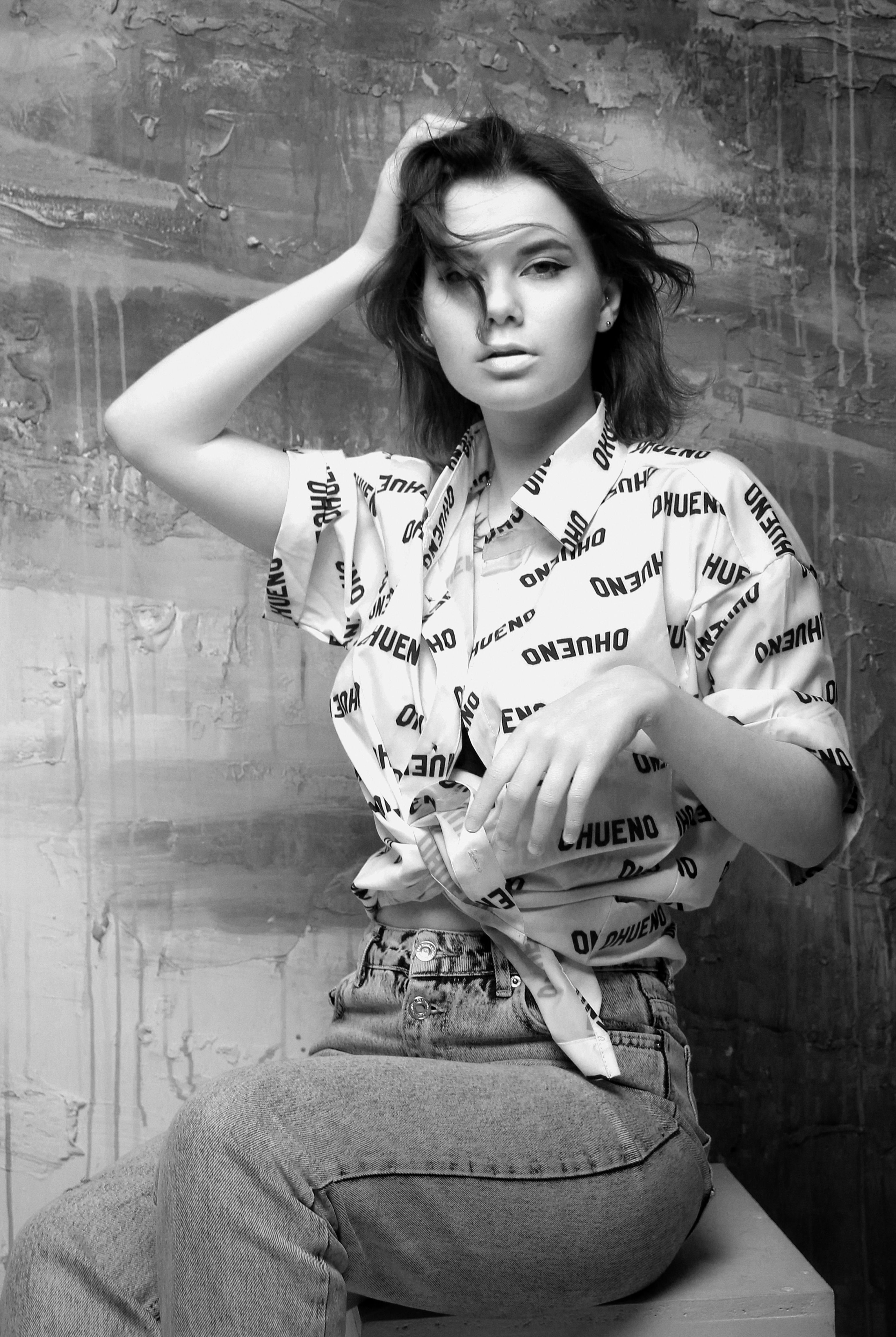 Artistic black and white portrait of a woman in casual wear, striking a pose indoors.