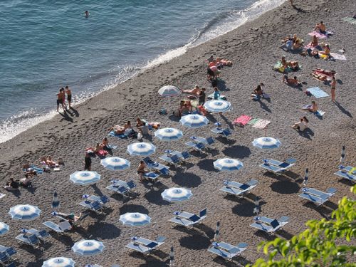 Free A bustling beach scene with sun umbrellas and sunbathers enjoying a sunny day. Stock Photo