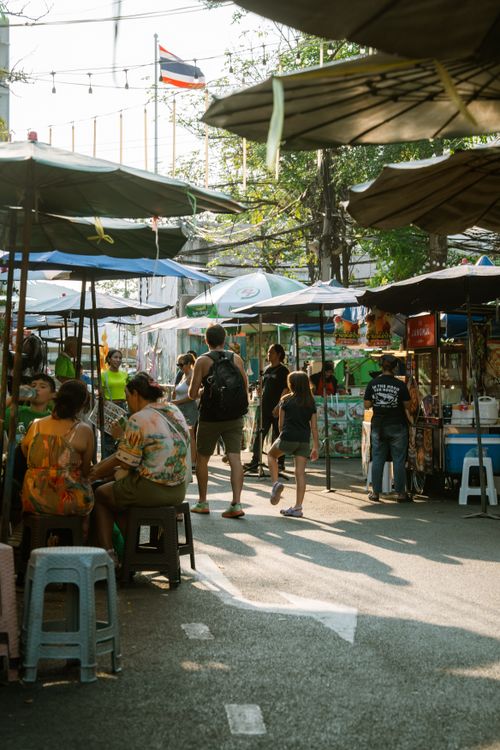 Free Discover the lively atmosphere of a bustling street market in Bangkok, Thailand, filled with vendors and diverse visitors under umbrellas. Stock Photo
