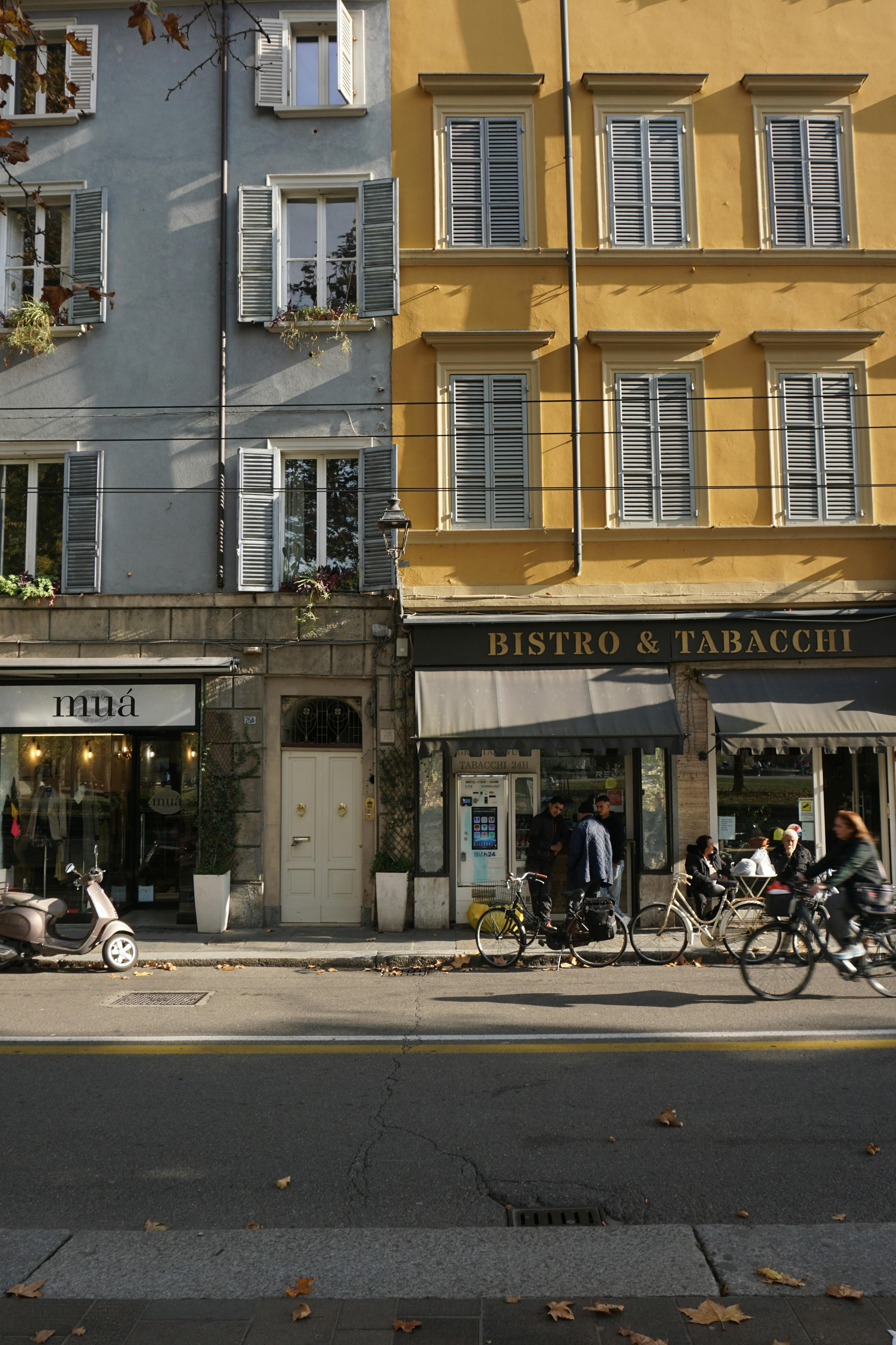 Cyclists pass by a bistro on a colorful street in Parma, Italy.