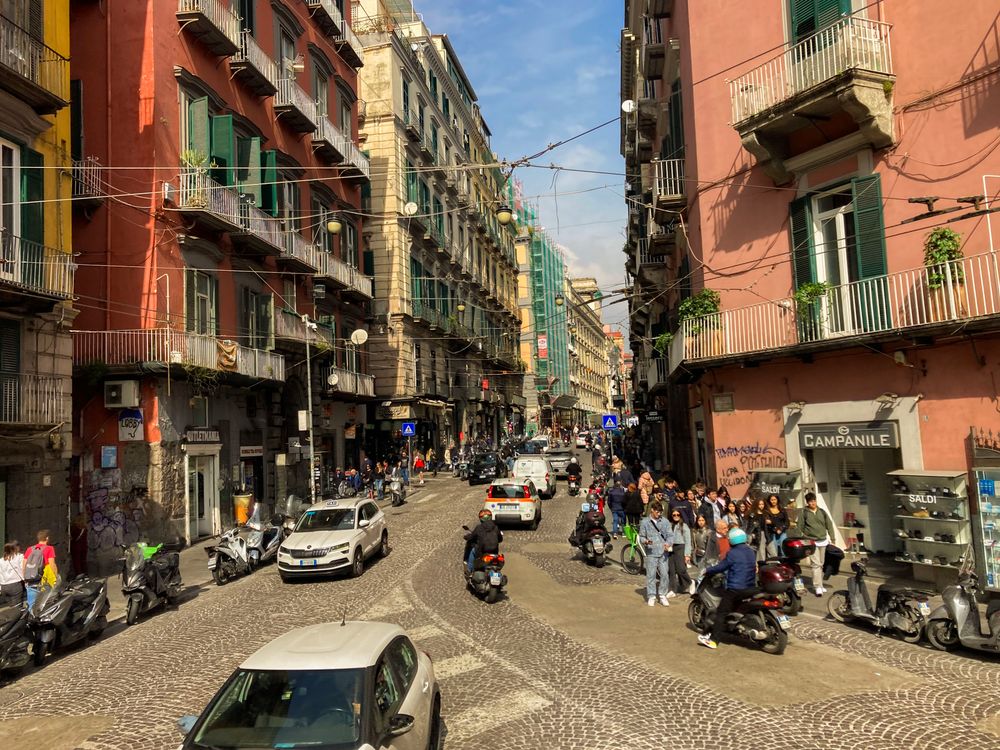 Stradă din Napoli cu scutere și pietoni, într-o zi însorită