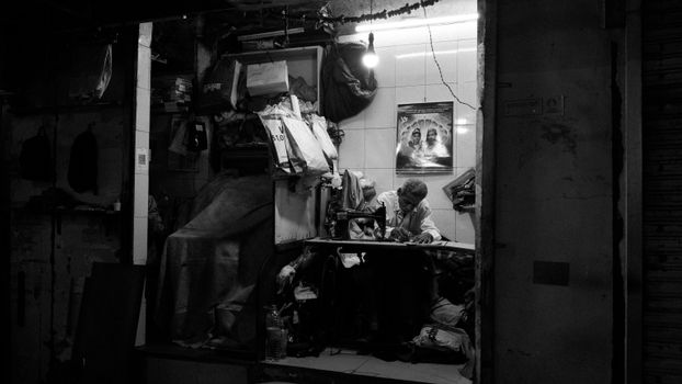 A dedicated tailor working at night in a cluttered Mumbai workshop, creating garments under warm light.
