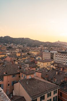 Captivating aerial view of Bologna's rooftops at sunset with rolling hills in the background.