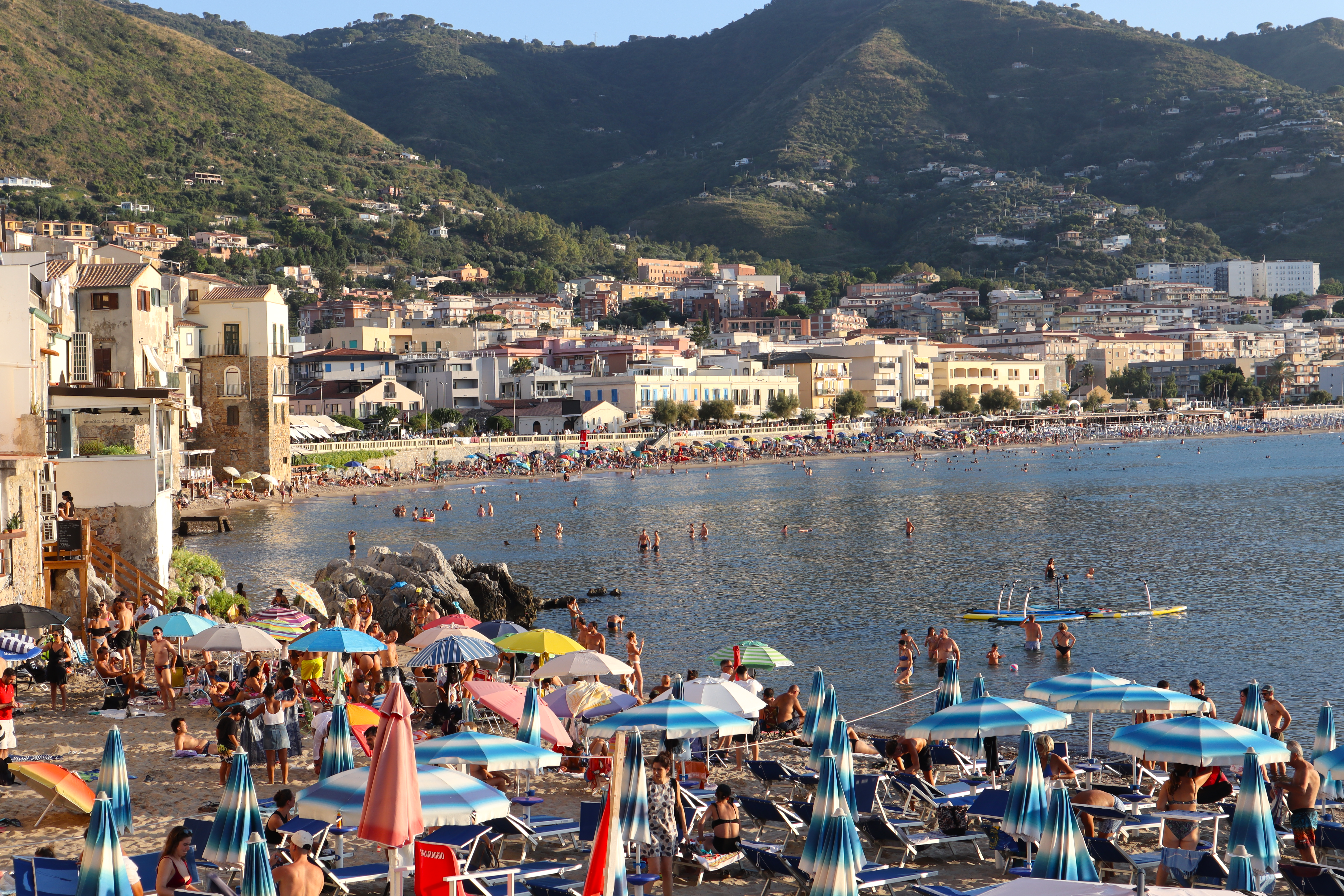 Vibrant summer day on Cefalù beach, Sicily with sunbathers and scenic coastal backdrop.
