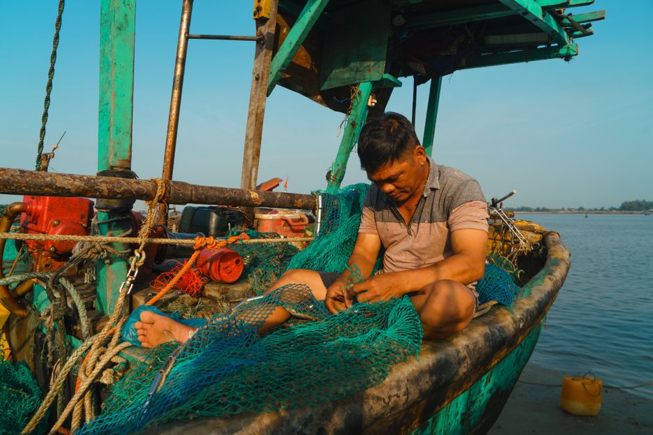 A fisherman repairs a net on his boat in Vũng Tàu, showcasing Vietnam's coastal lifestyle.