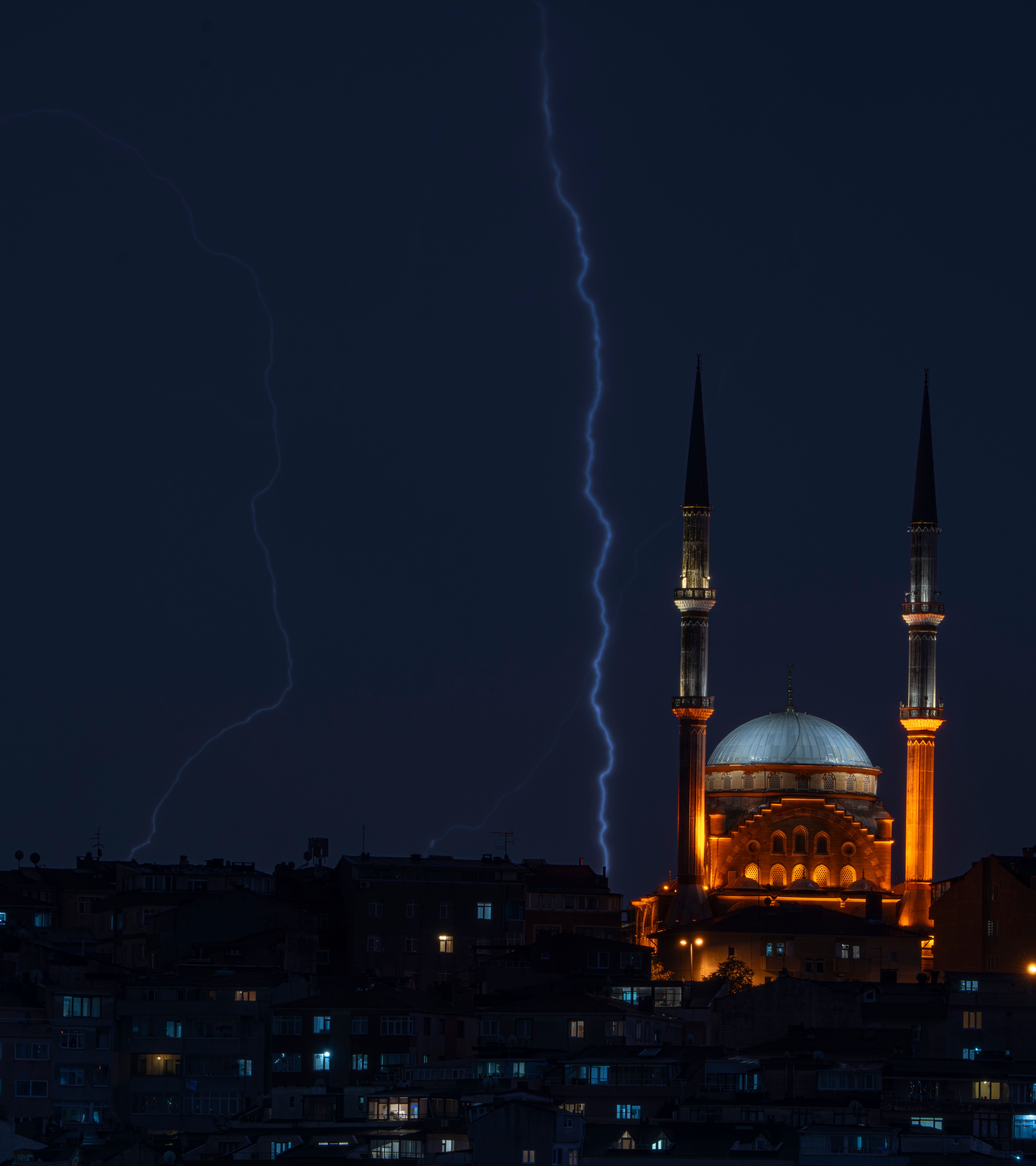 A stunning view of a mosque in Istanbul illuminated against a stormy night sky with lightning.