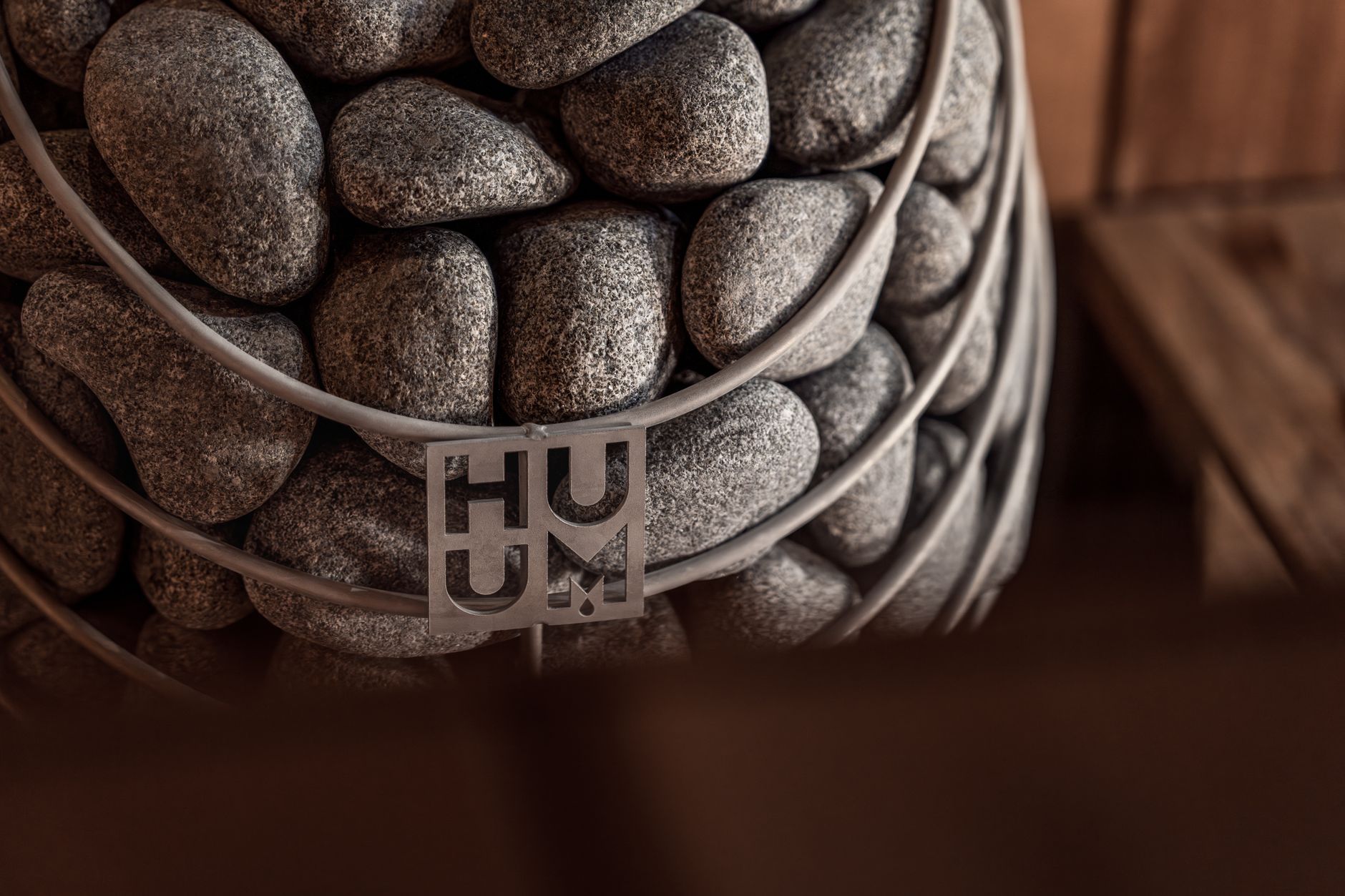 Close-up of a modern sauna heater stacked with smooth stones in a wooden cabin setting.