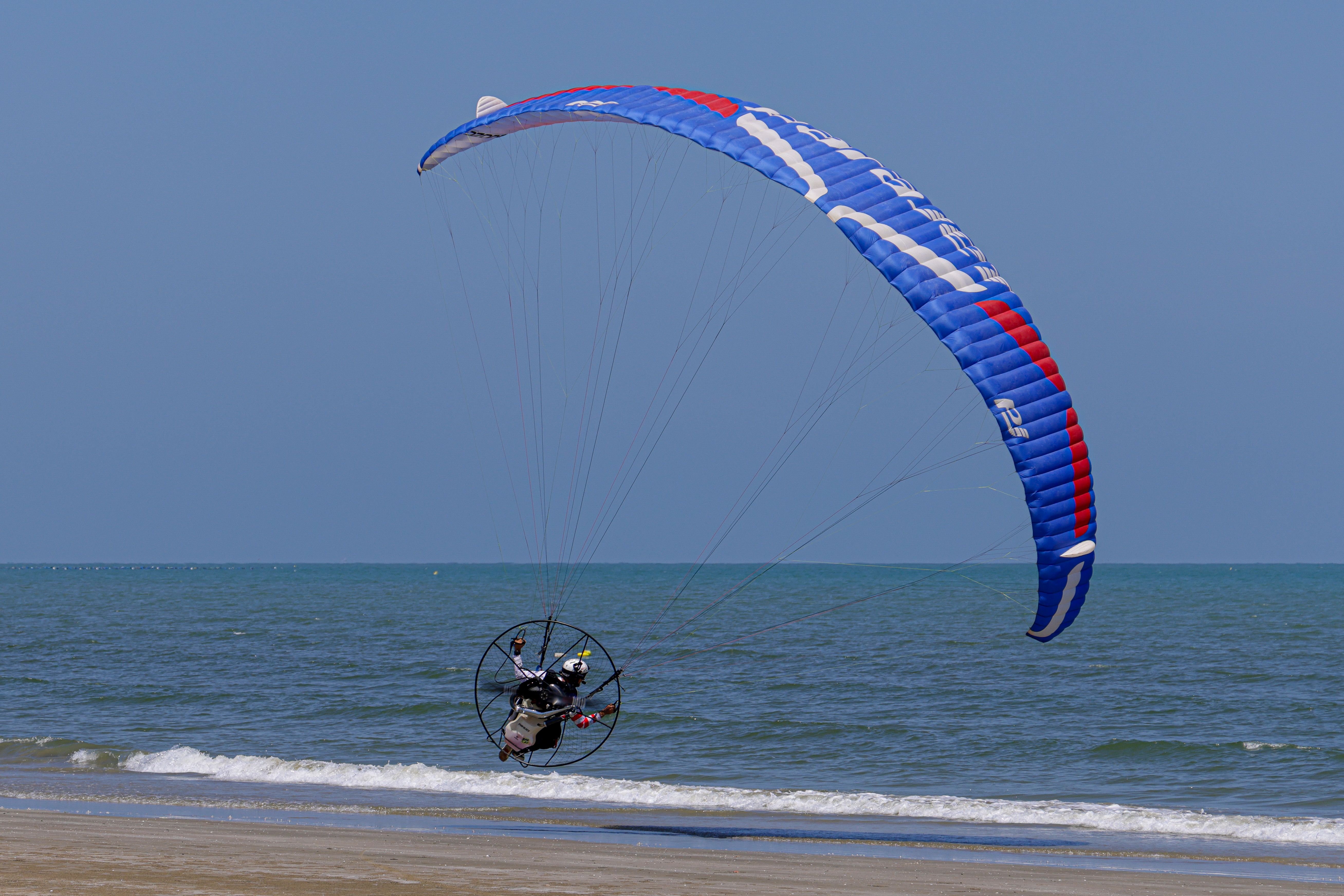 Stunning image of a paramotor gliding over a beach with clear blue skies.