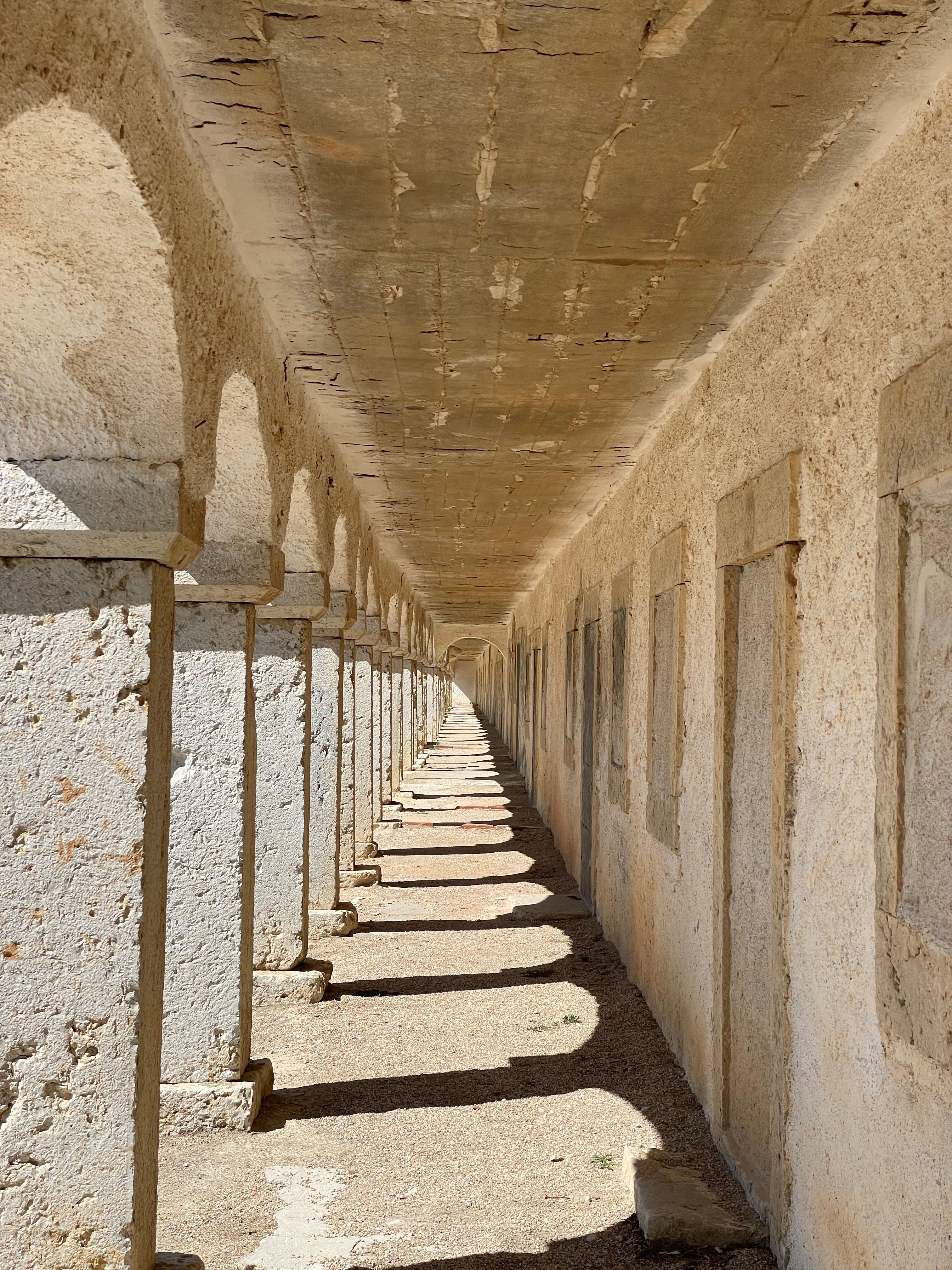 A sunlit stone corridor featuring repeating arches creates a striking ancient architectural perspective.