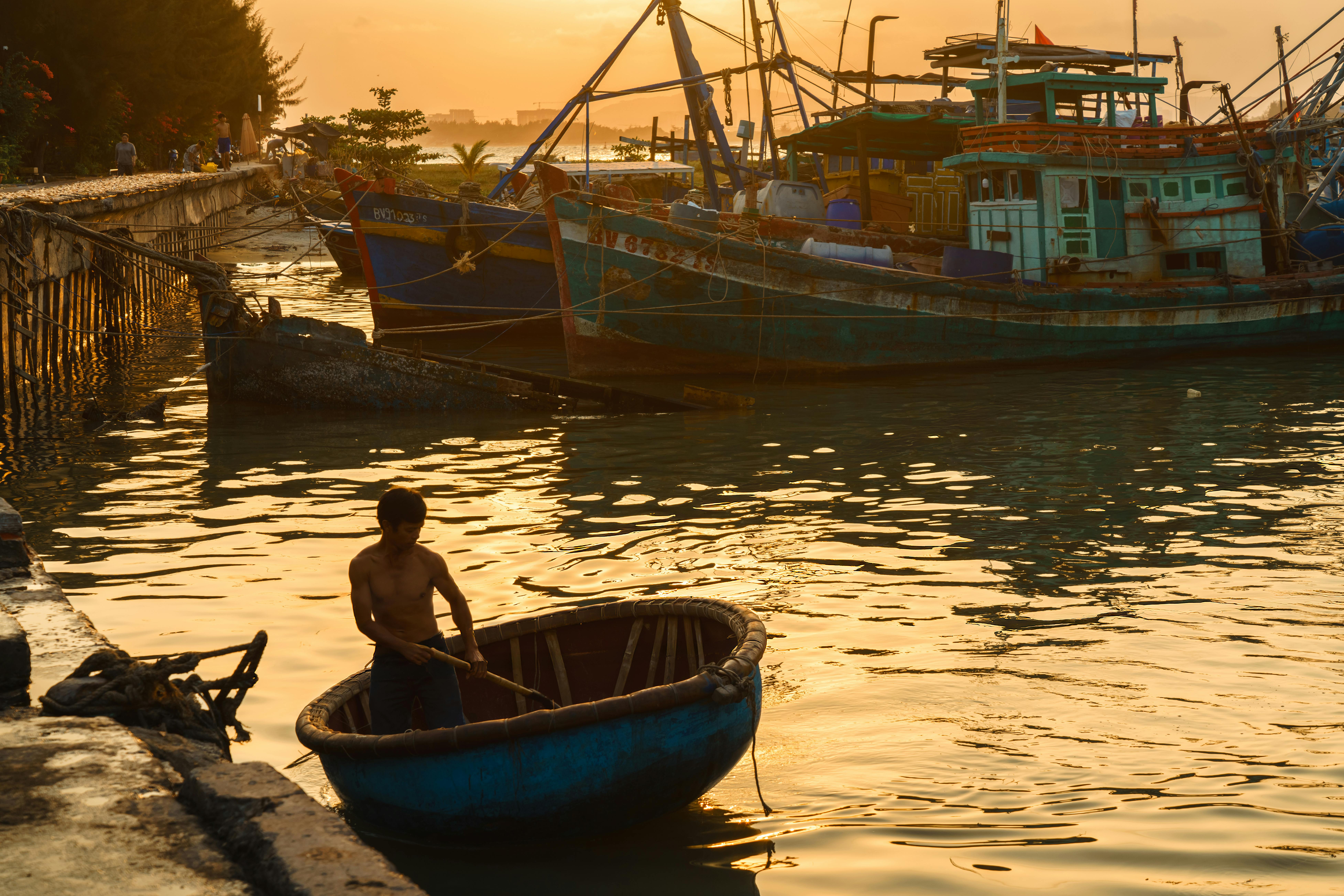 Silhouetted fisherman rowing basket boat in Vũng Tàu at sunset.
