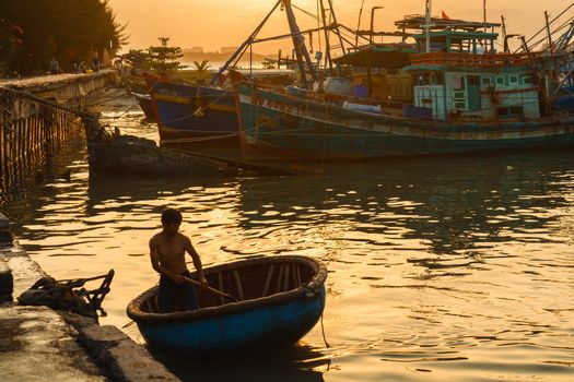 Silhouetted fisherman rowing basket boat in Vũng Tàu at sunset.