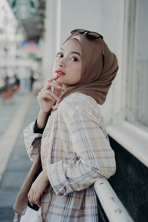 Mulher Em Hijab Marrom E Branco Marrom E Xadrez Branco Camisa De Manga Longa Apoiada Em Uma Grade De Metal