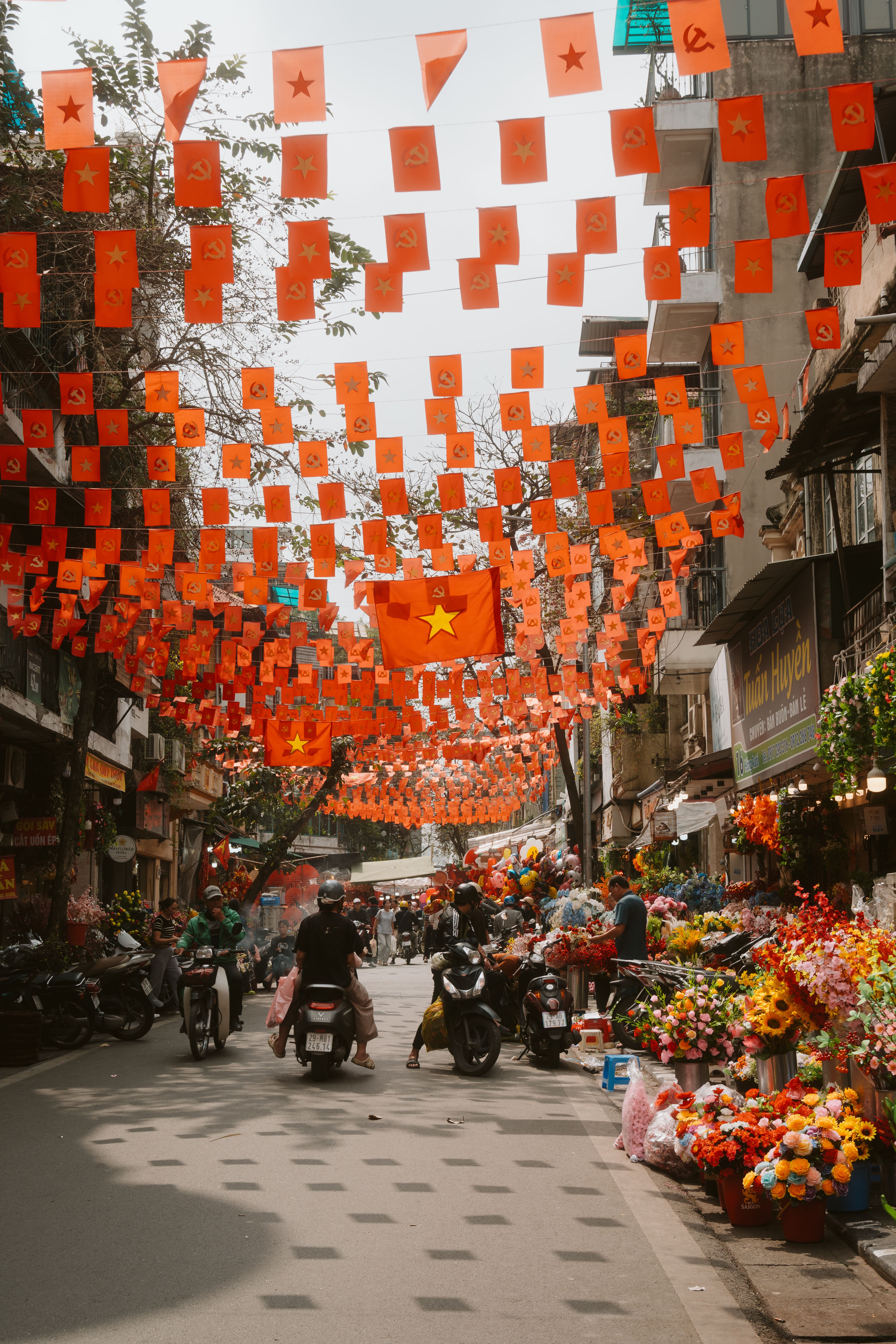 A bustling Vietnamese street adorned with orange flags, lively vendors, and motorbikes, capturing the essence of local life.