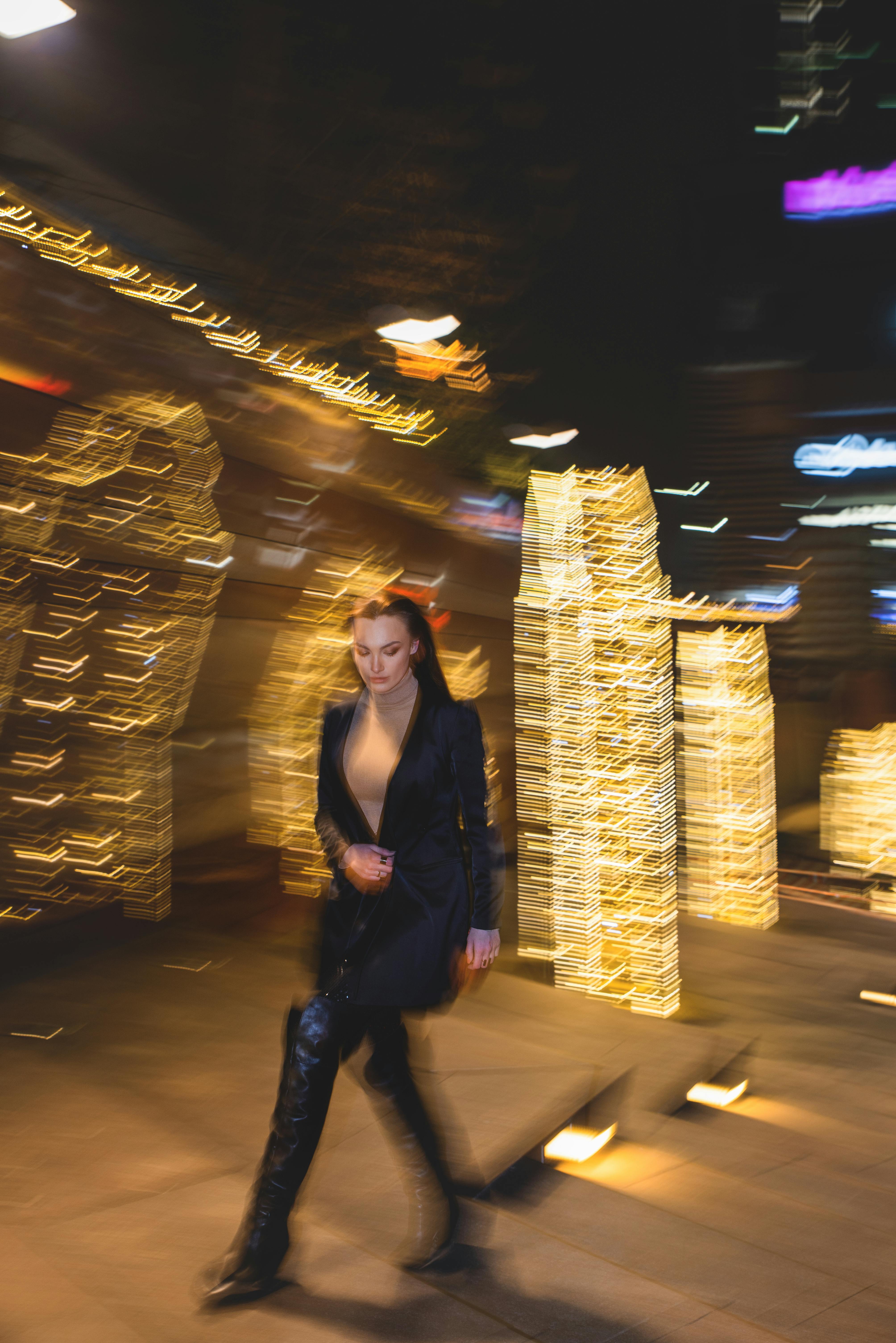 Dynamic image of woman walking in city with festive lights creating bokeh effect.