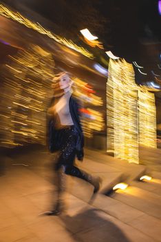 Artistic blur photograph of a woman walking with city lights in background at night.