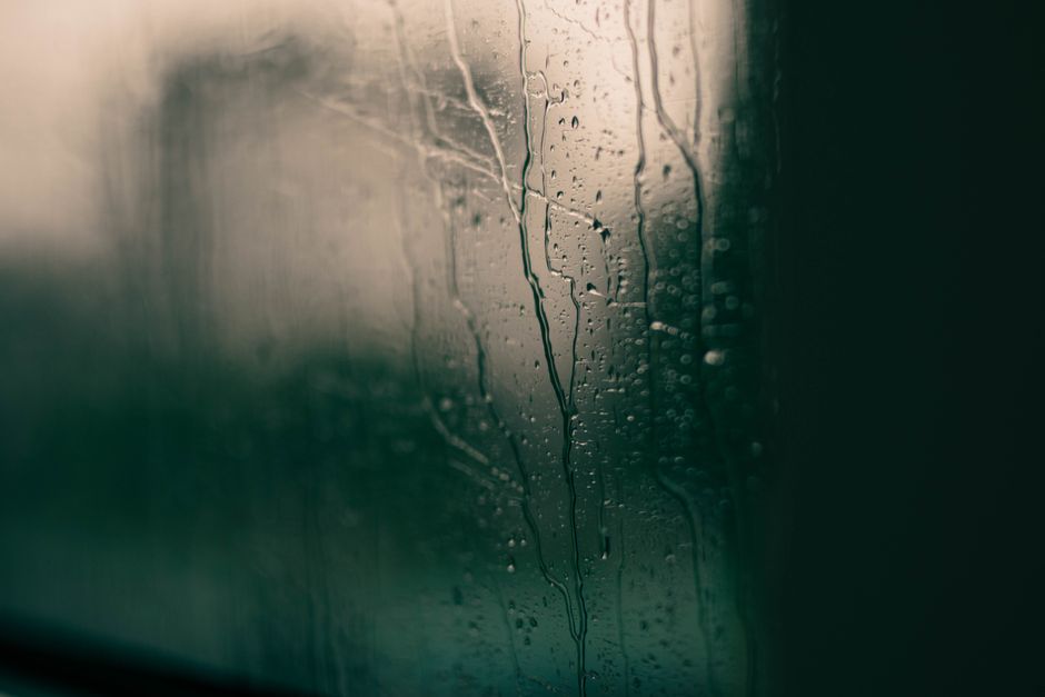 Water droplets and condensation streaming down an interior window pane with a moody dark atmosphere.