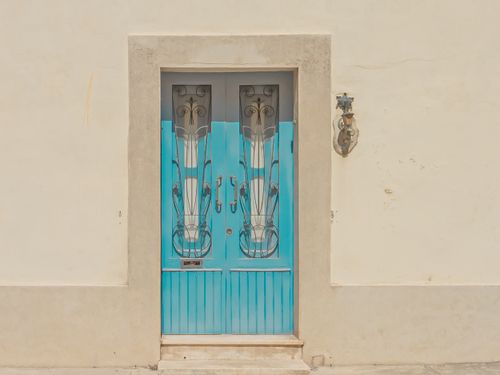 Free A blue double door with intricate ironwork set in a white plaster wall, offering a charming architectural detail. Stock Photo