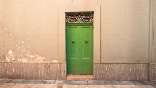 Free A vibrant green door set in a worn city wall with an ornate grille, perfect for urban exploration themes. Stock Photo