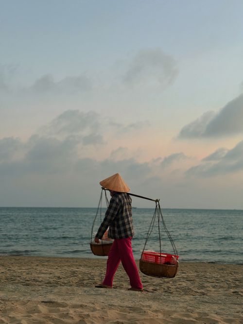 Free A Vietnamese vendor with a conical hat carrying baskets on a beach in Phan Thiet at sunset. Stock Photo