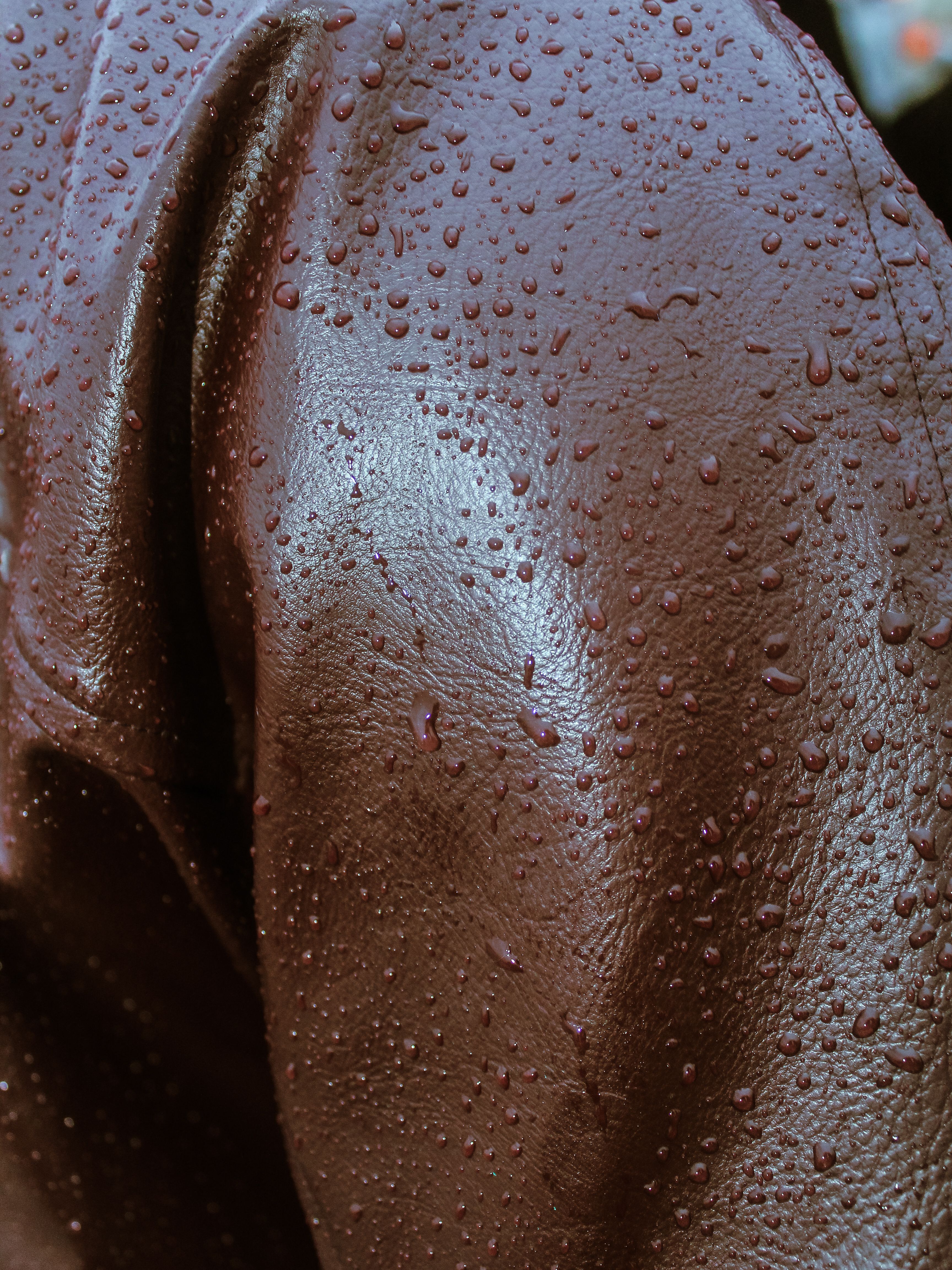 Detailed texture of a brown leather jacket with raindrops, capturing the essence of wet weather fashion.